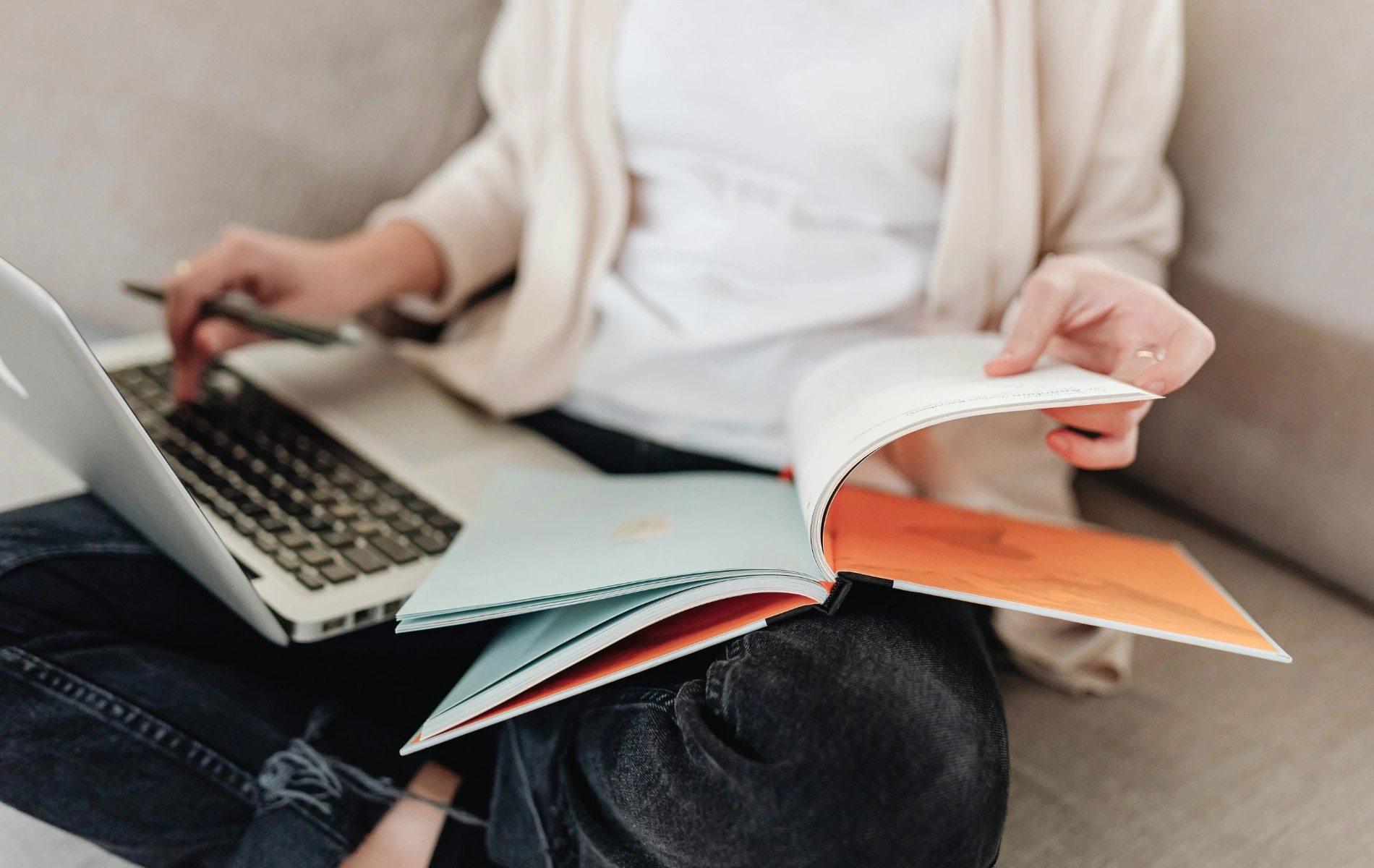 Frau die in einem Buch blättert und dabei einen Laptop vor sich hat.